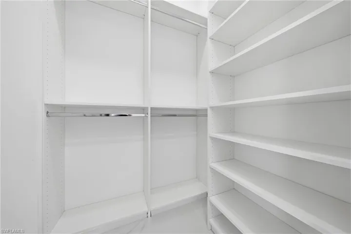 White walk-in closet featuring built-in shelving, chrome hanging rods, and light-toned flooring
