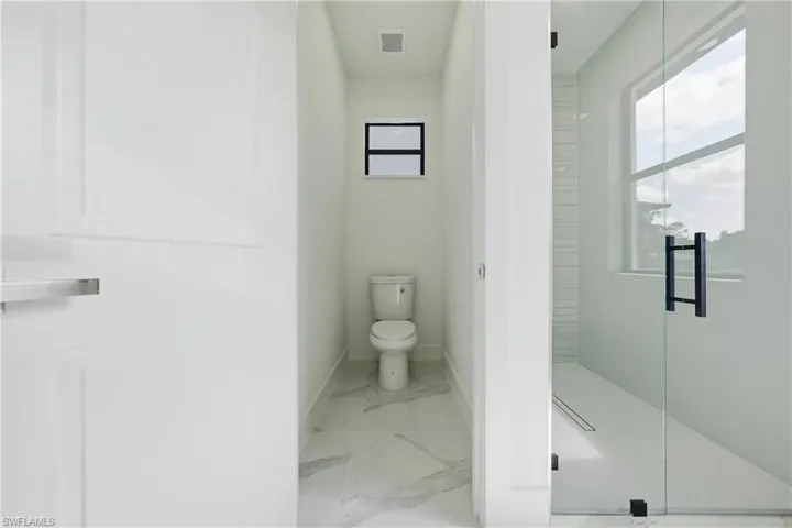 Modern bathroom featuring a glass-enclosed shower with matte black hardware, a toilet alcove with a window, and large format tile flooring