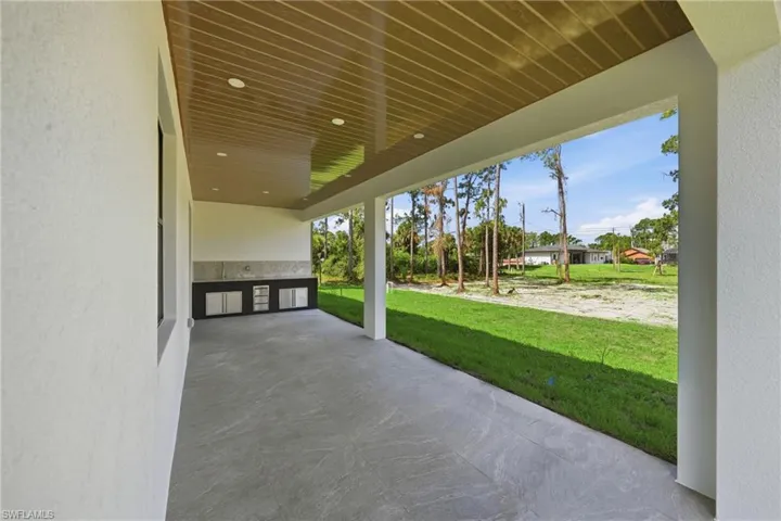 Expansive covered patio featuring a textured concrete floor, recessed lighting, and a detailed wood-finish ceiling