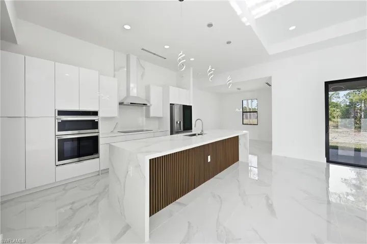 Modern kitchen featuring a waterfall island with wood-finish paneling, white gloss cabinetry, integrated double ovens, and a contemporary range hood