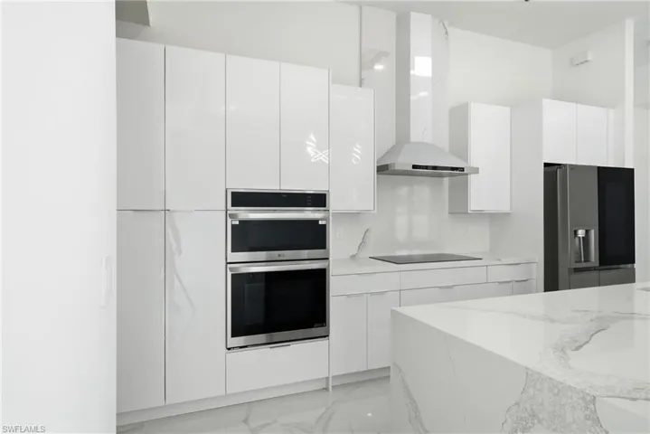 Contemporary kitchen featuring white high-gloss cabinetry, built-in double ovens, a stainless steel range hood, and a large center island with a waterfall countertop