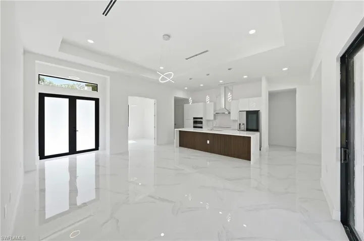 Spacious open-concept interior featuring large format marble-look tile flooring, white walls, and a recessed ceiling with integrated lighting
