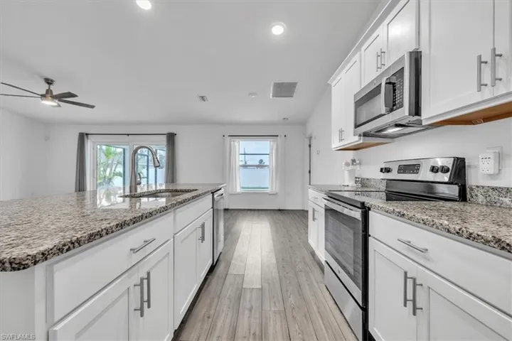 Kitchen featuring stainless steel appliances, white cabinets, and light stone countertops