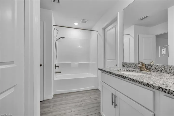 Bathroom featuring light wood finished floors, vanity,  shower combination, and recessed lighting