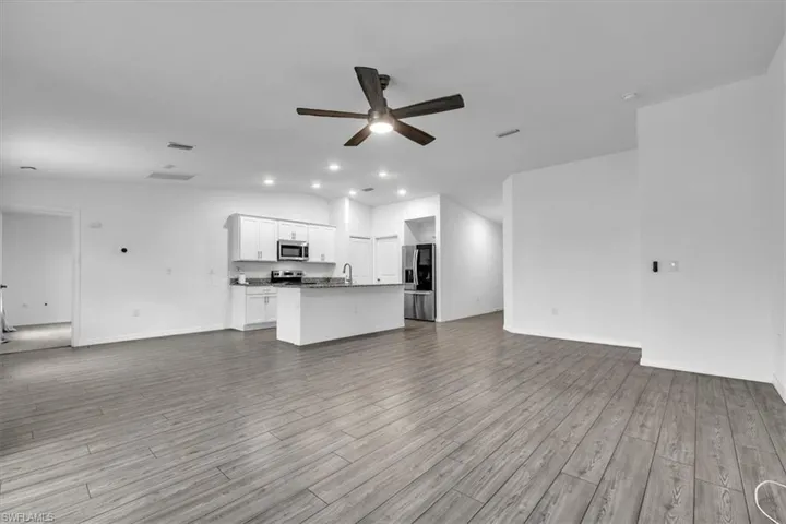 Kitchen with stainless steel appliances, white cabinets, dark stone countertops, an island with sink, and open floor plan