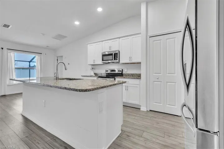 Kitchen with white cabinetry, dark stone countertops, stainless steel appliances, light wood-style flooring, and vaulted ceiling