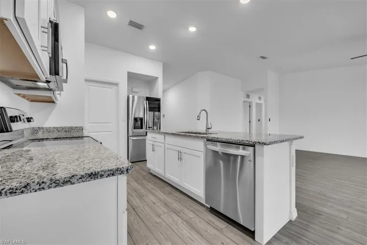 Kitchen featuring lofted ceiling, stainless steel appliances, light stone counters, white cabinets, and a kitchen island with sink