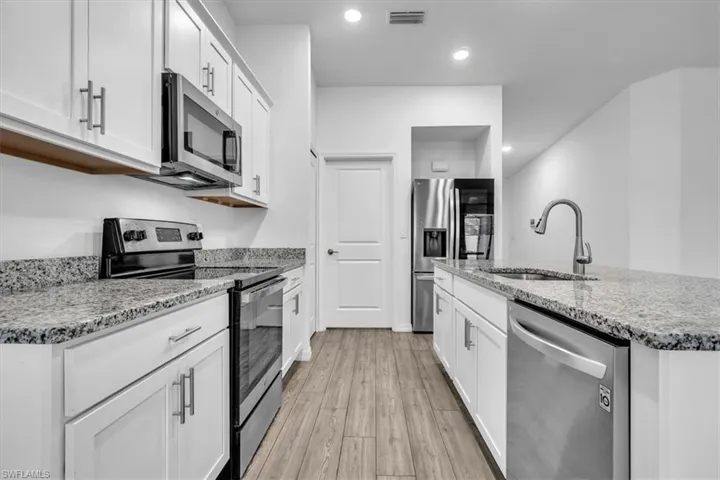 Kitchen featuring stainless steel appliances, white cabinets, light stone countertops, light wood finished floors, and an island with sink