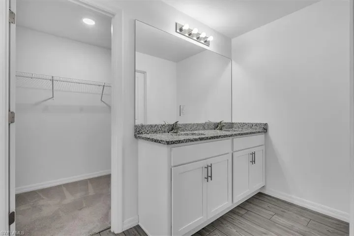 Full bath with double vanity, a spacious closet, and light wood finished floors