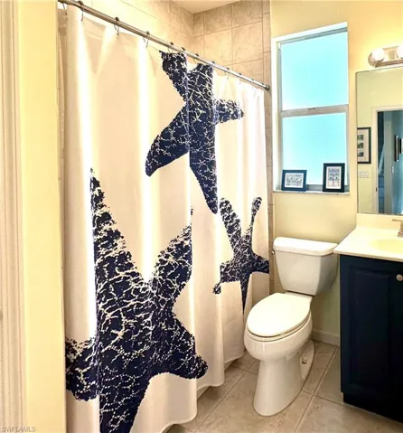 Guest bathroom with vanity, curtained shower, and light tile patterned floors.