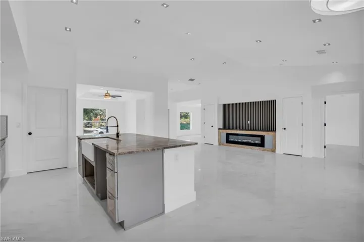 Kitchen with dark stone countertops, an island with sink, ceiling fan, and light tile floors
