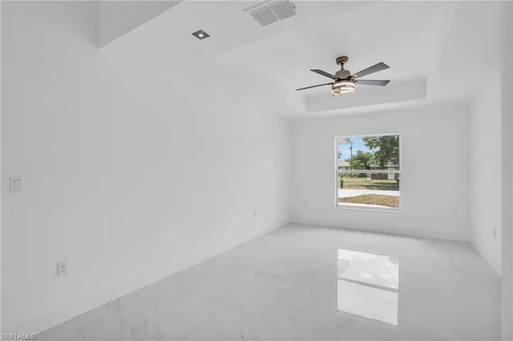 Empty room featuring a raised ceiling, ceiling fan, and light tile floors