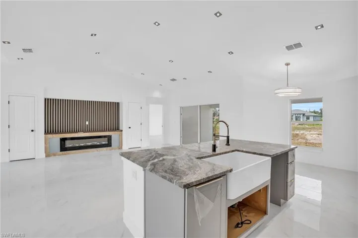 Kitchen with a center island with sink, light stone counters, vaulted ceiling, and light tile floors
