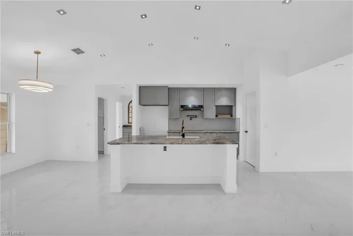 Kitchen featuring dark stone countertops, a kitchen island with sink, gray cabinets, sink, and light tile flooring