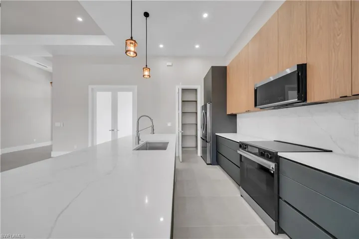 Kitchen with modern cabinets, appliances with stainless steel finishes, light stone counters, pendant lighting, and recessed lighting