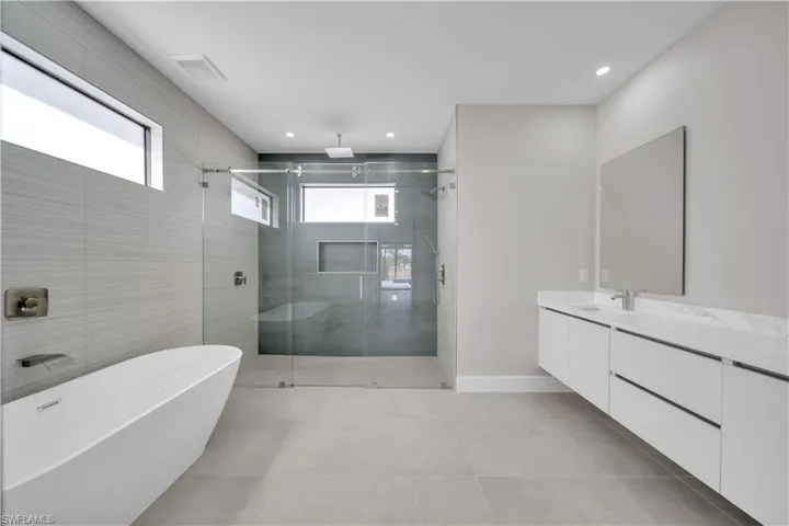 Full bath with vanity, a stall shower, a freestanding tub, light tile patterned floors, and recessed lighting