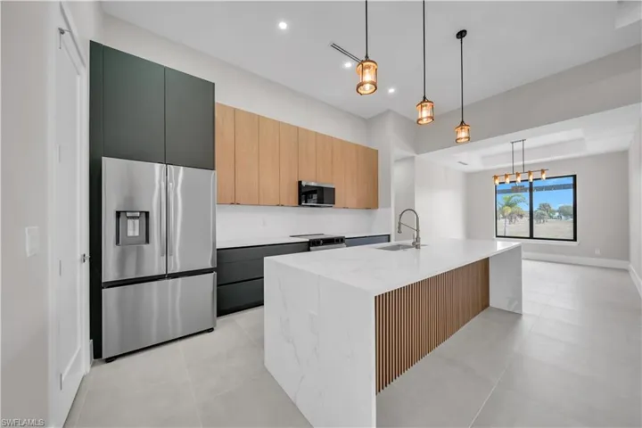 Kitchen with appliances with stainless steel finishes, modern cabinets, hanging light fixtures, light tile patterned flooring, and light stone countertops