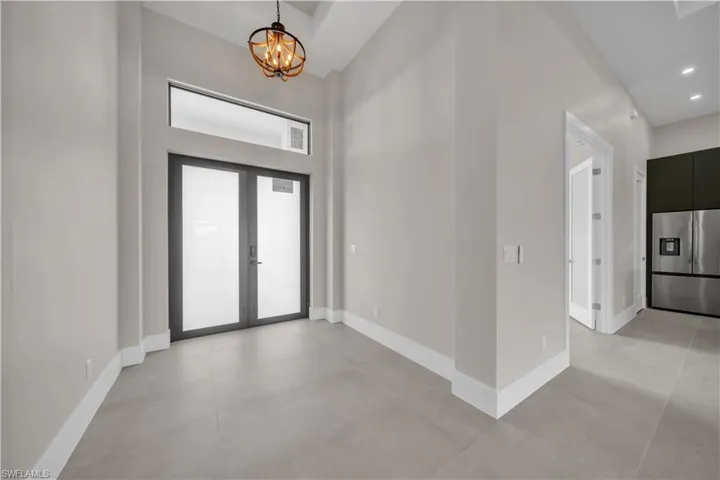 Foyer with a high ceiling, concrete floors, a chandelier, french doors, and recessed lighting