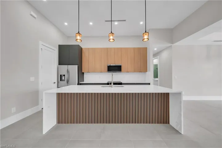 Kitchen with modern cabinets, decorative light fixtures, a large island with sink, light stone counters, and appliances with stainless steel finishes