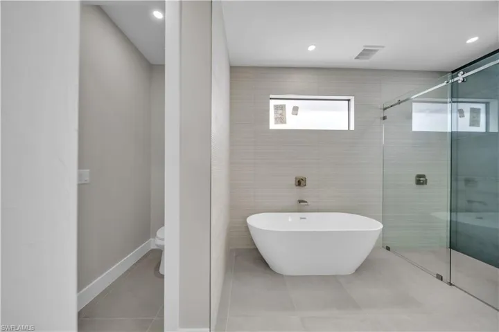 Bathroom featuring a shower stall, a freestanding tub, tile walls, tile patterned floors, and recessed lighting