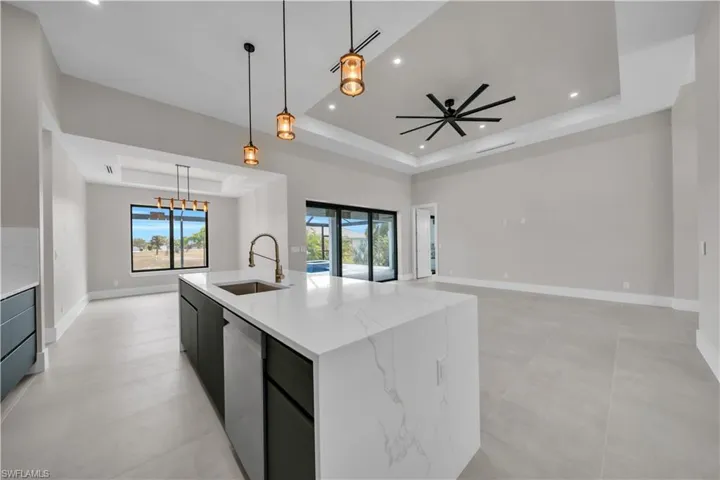 Kitchen featuring a tray ceiling, modern cabinets, hanging light fixtures, light stone countertops, and dishwasher