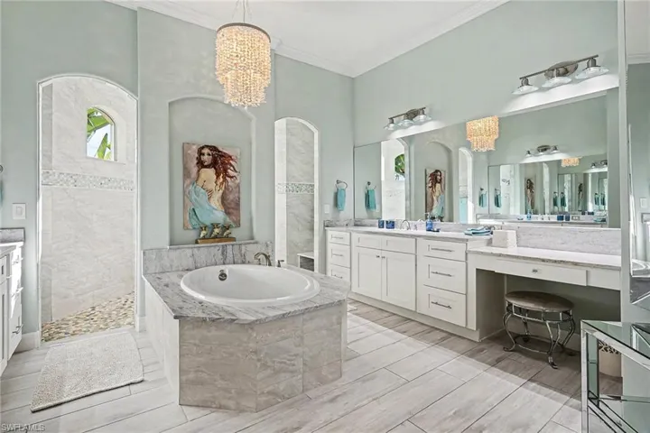 Bathroom featuring a garden tub, vanity, crown molding, walk in shower, and a chandelier