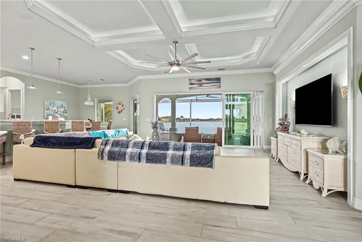 Living room featuring coffered ceiling, crown molding, a ceiling fan, wood finish floors, and arched walkways