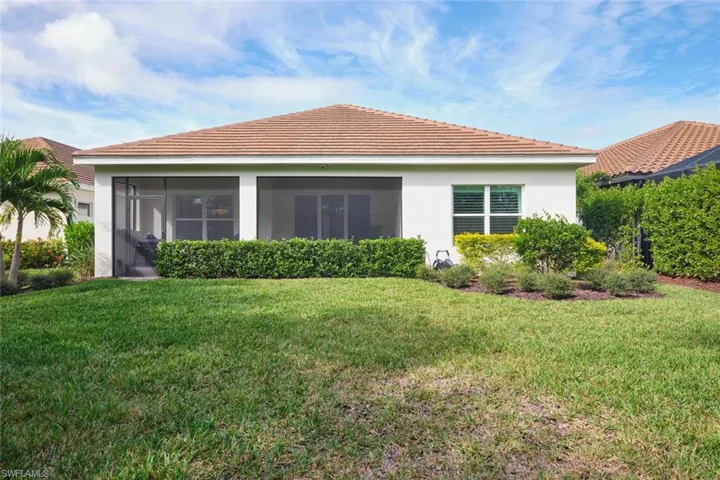 Back of property featuring a lawn, stucco siding, a sunroom, and a tile roof