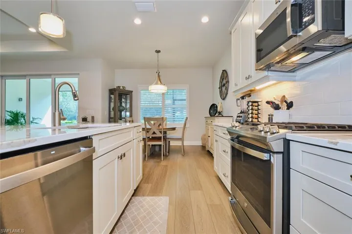 Kitchen featuring appliances with stainless steel finishes, white cabinets, decorative light fixtures, light stone counters, and light wood-type flooring