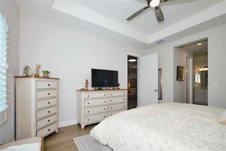 Bedroom with light wood-style flooring, a ceiling fan, recessed lighting, ensuite bathroom, and a tray ceiling