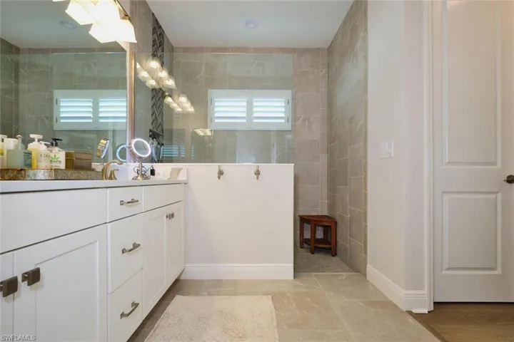 Bathroom with vanity, a walk in shower, and tile walls