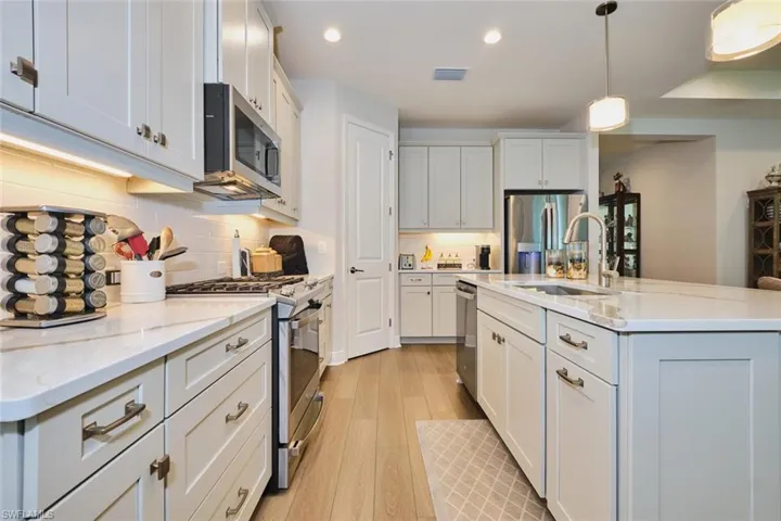 Kitchen with appliances with stainless steel finishes, light wood finished floors, recessed lighting, an island with sink, and hanging light fixtures