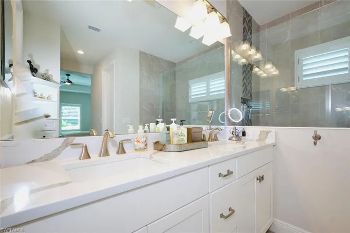 Bathroom featuring healthy amount of natural light, walk in shower, double vanity, and a ceiling fan