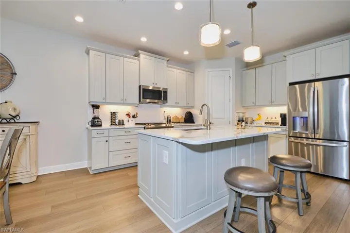 Kitchen featuring appliances with stainless steel finishes, light wood finished floors, a kitchen island with sink, a breakfast bar, and pendant lighting