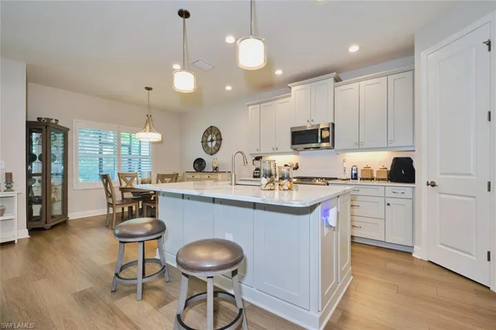 Kitchen featuring a kitchen bar, white cabinets, light wood-style floors, an island with sink, and stainless steel microwave