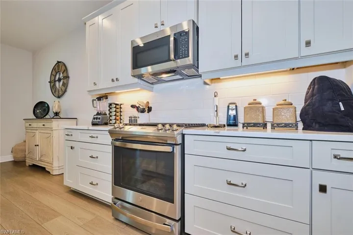Kitchen featuring stainless steel appliances, white cabinets, light wood-type flooring, backsplash, and light stone counters
