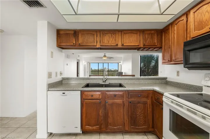 Kitchen with ceiling fan, white appliances, sink, and light tile patterned floors
