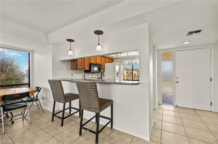 Kitchen with a breakfast bar, white fridge with ice dispenser, hanging light fixtures, and light tile patterned floors