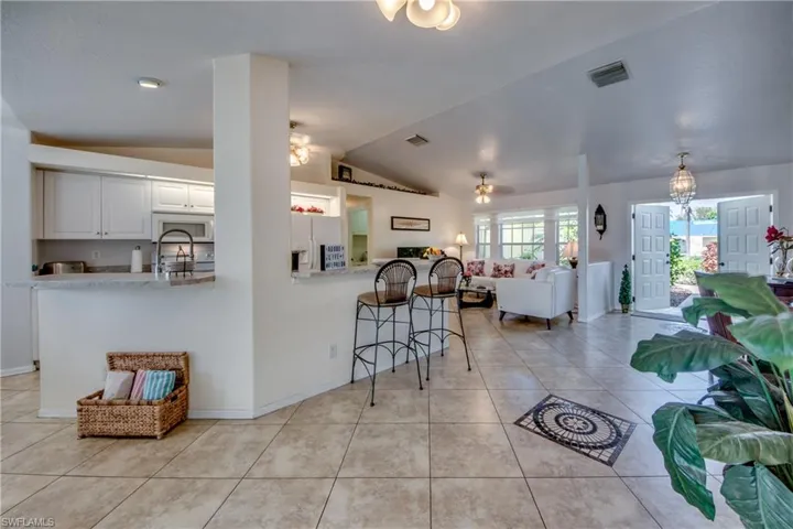 Kitchen with white appliances, lofted ceiling, white cabinets, light tile patterned floors, and kitchen peninsula