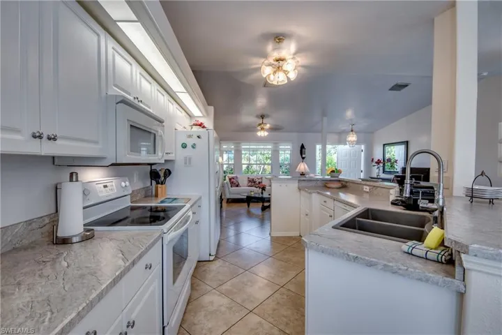 Kitchen featuring kitchen peninsula, white appliances, vaulted ceiling, sink, and white cabinets