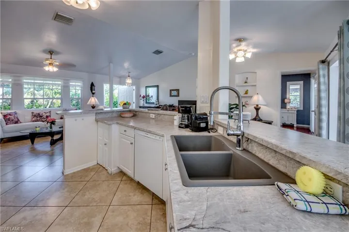 Kitchen featuring white cabinetry, white dishwasher, a healthy amount of sunlight, and vaulted ceiling