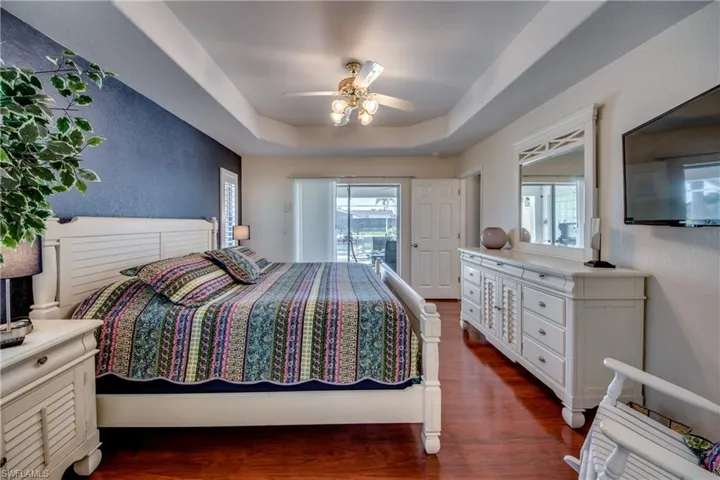 Bedroom with a tray ceiling, multiple windows, ceiling fan, and dark hardwood / wood-style flooring