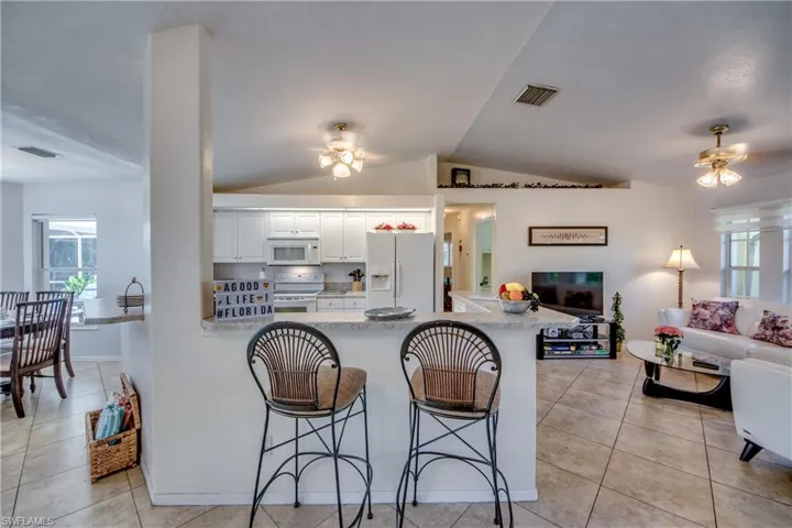 Kitchen featuring a kitchen breakfast bar, lofted ceiling, white cabinets, and white appliances