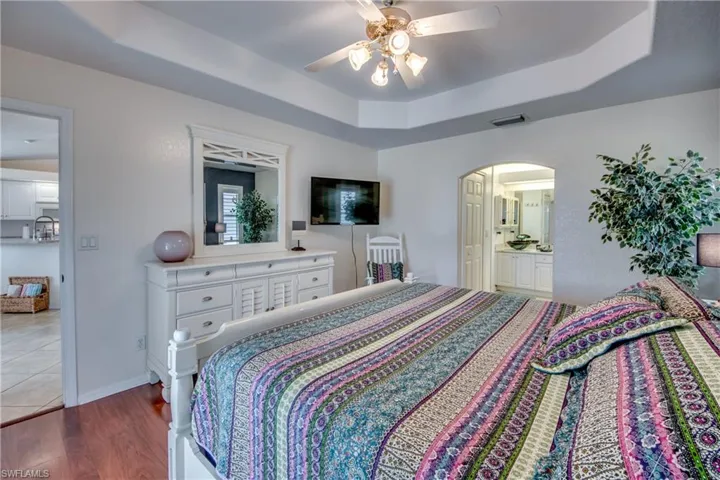 Bedroom featuring ceiling fan, a raised ceiling, connected bathroom, and light hardwood / wood-style flooring