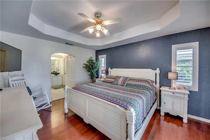 Bedroom featuring dark hardwood / wood-style flooring, a tray ceiling, ensuite bath, and ceiling fan