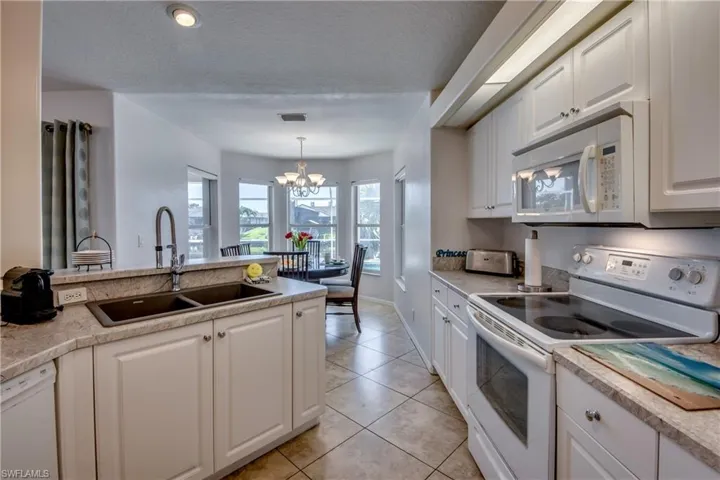 Kitchen featuring a textured ceiling, white appliances, sink, a chandelier, and white cabinetry
