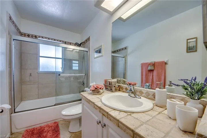 Full bathroom with a skylight, enclosed tub / shower combo, tile patterned floors, toilet, and vanity