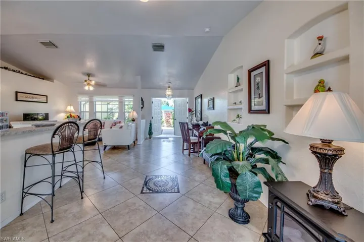 Tiled living room featuring ceiling fan, built in features, and vaulted ceiling