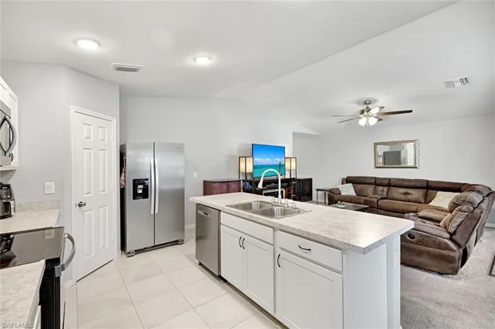 Kitchen with white cabinetry, stainless steel appliances, light countertops, open floor plan, and a center island with sink