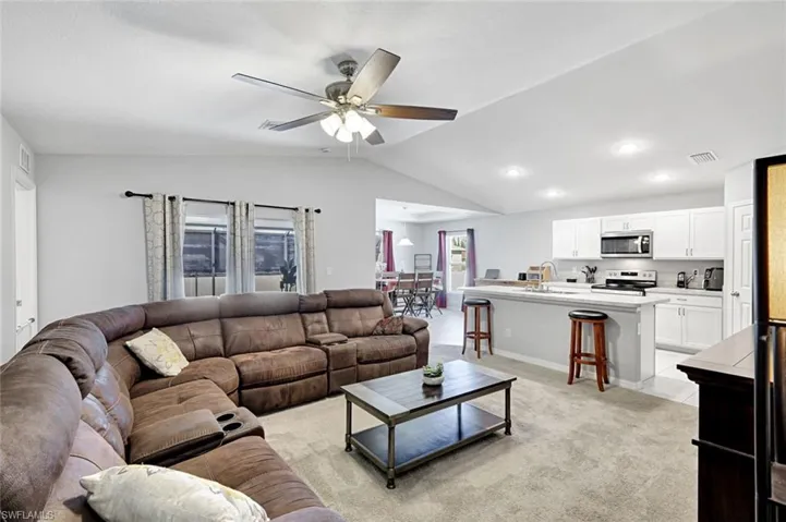 Living area with light colored carpet, lofted ceiling, and ceiling fan